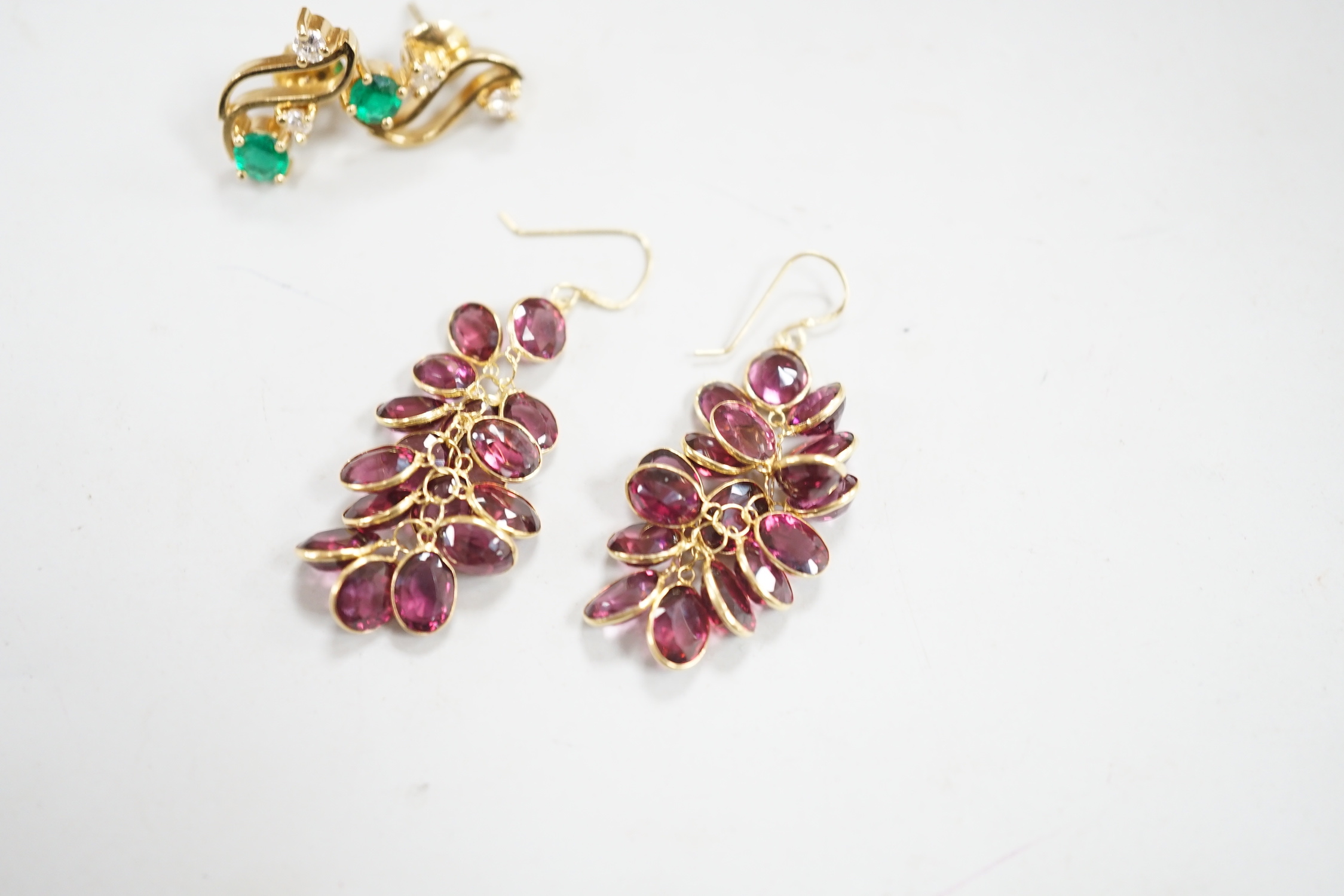 A modern pair of yellow metal, emerald and diamond set three stone ear studs, 14mm and a modern pair of yellow metal and garnet cluster set drop earrings, gross weight 8.3 grams.